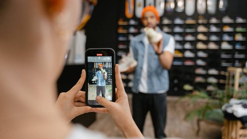 Person videoing a man for social media in a clothing store.