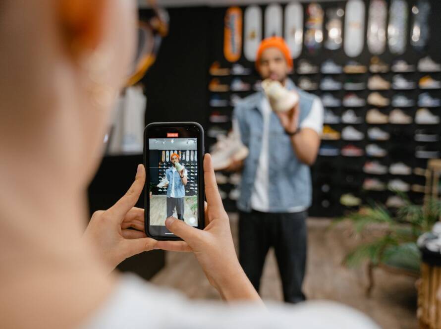 Person videoing a man for social media in a clothing store.